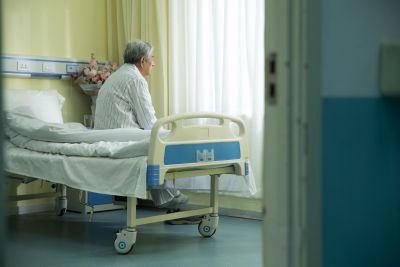 Elderly Chinese man siting on the edge of a bed