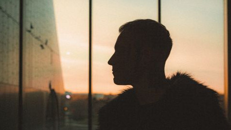 Backlit person standing in front of a window with features obscured by the light.