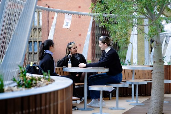 Three people sit around a table next to a tree on one of the Arts and Cultural building balconies.