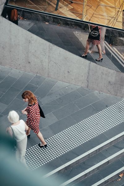 Two women walking down the stairs in a concerted space. Their reflection is captured in a reflective wall beside them.