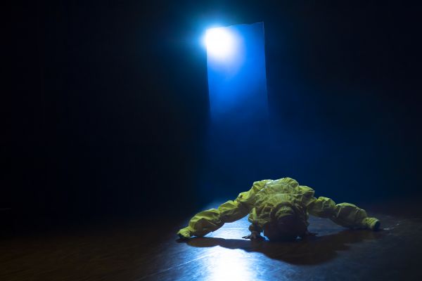 A dancer in a yellow costume performs under a blue light.