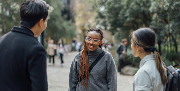 A group of young alumni conversing in a tree-lined path.