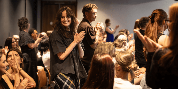 An alumni group giving applause to a speaker at an event. Some are sitting and others are standing.