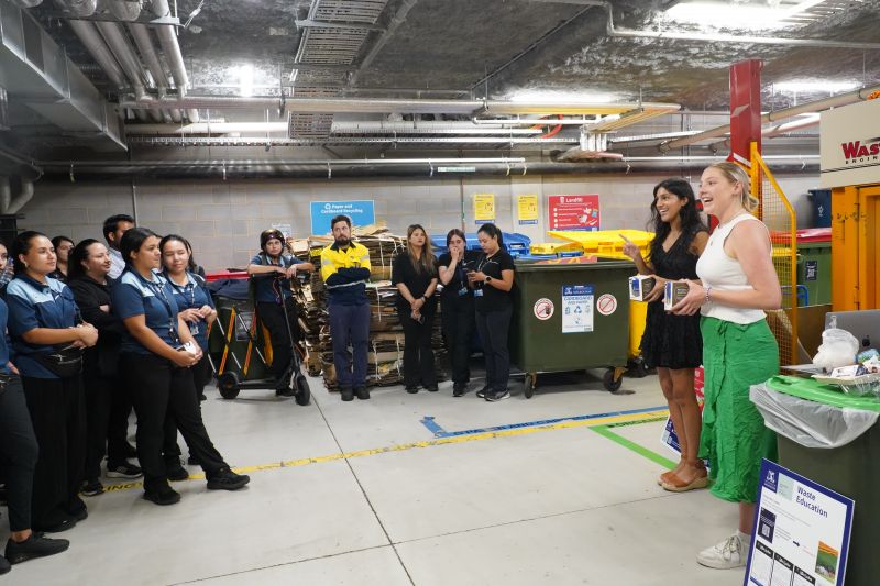 A dark haired woman and a blonde woman instructing cleaning staff at the Waste Hub in the Arts and Cultural Building.