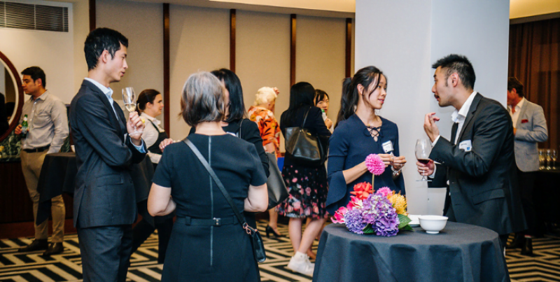 A group of alumni mingling with drinks in hand at a Beijing Alumni Association event.