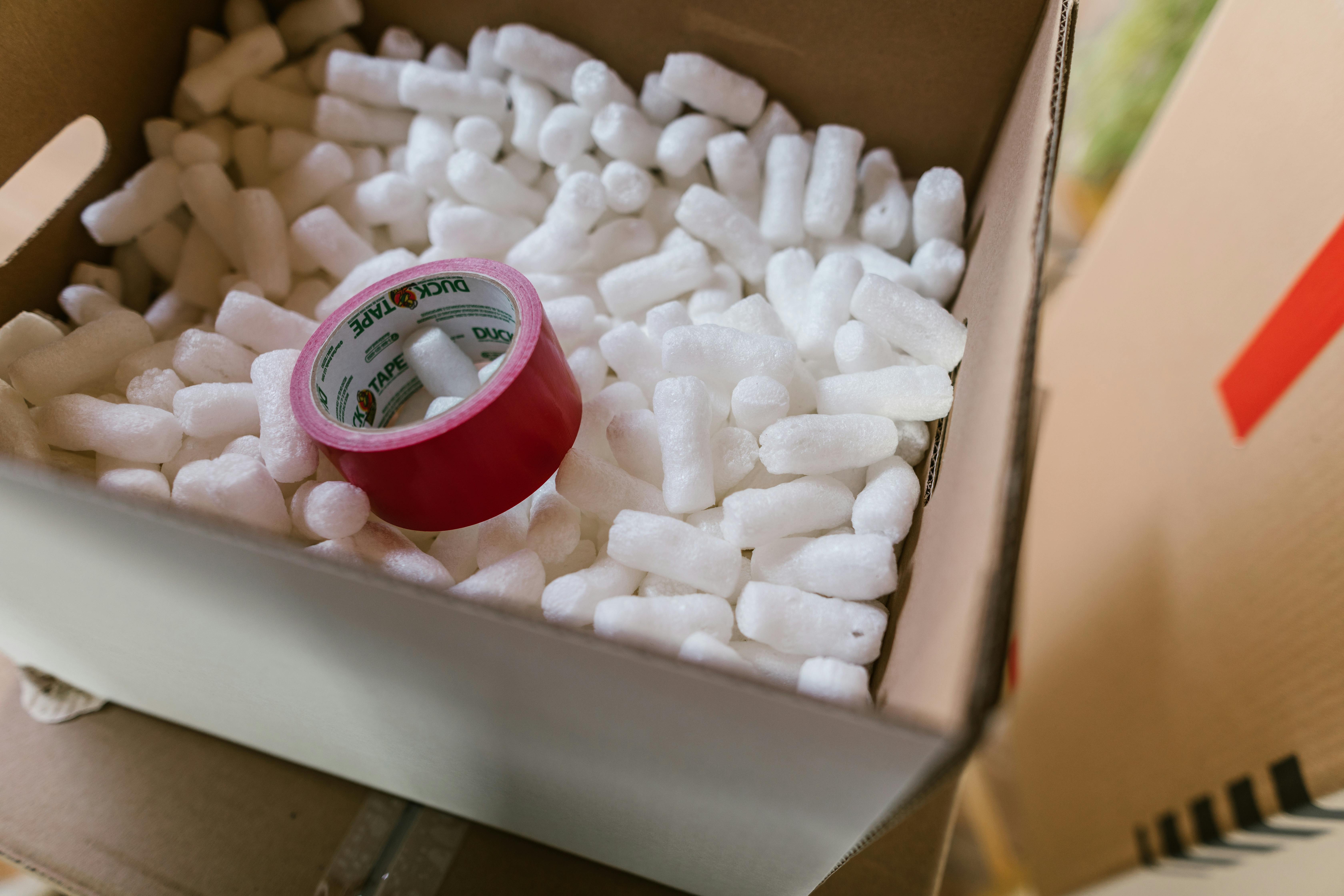 A brown cardboard box with polystyrene pellets and a roll of packing tape