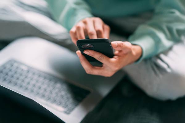 a person holding a mobile phone with a notebook computer in their lap