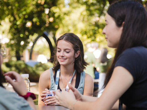 A Narrm scholar is sitting with some friends in an outdoor setting.