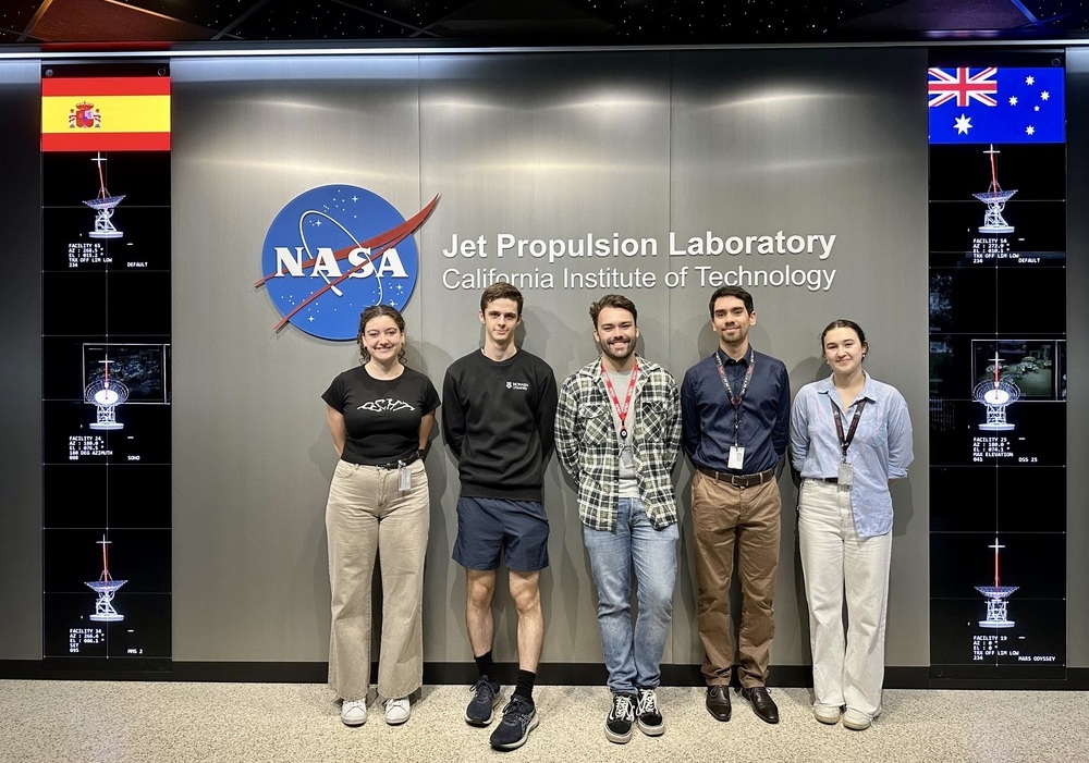 Five people smiling in front of a NASA sign at a space laboratory. 