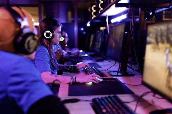 A girl at a desktop gaming setup in a dim yet colourfully lit room