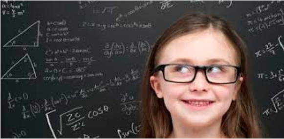Image of a young smiling girl pictured in front of a blackboard filled with mathematic equations.