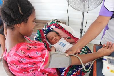 A young woman getting her blood pressure tested, with her newborn baby laying on her lap