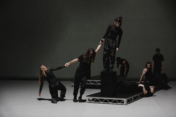 Dancers, dressed in black, strike poses while holding hands.