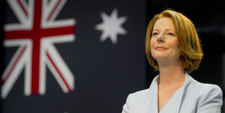 Julia Gillard in front of the Australian flag, smiling thoughtfully into the distance.