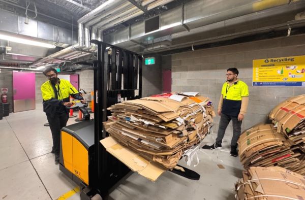 Two dark-haired Waste Monitors, Asim and Abi, collecting and transporting cardboard to the Waste Hub at the Arts and Cultural Building.