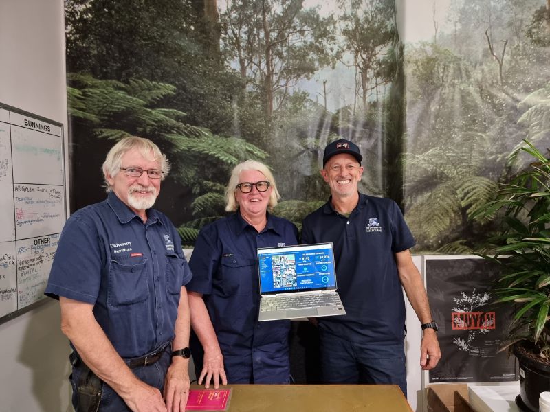 Three smiling Parkville grounds team member holding a laptop depicting the completion of initial data collection of plant records in 2023