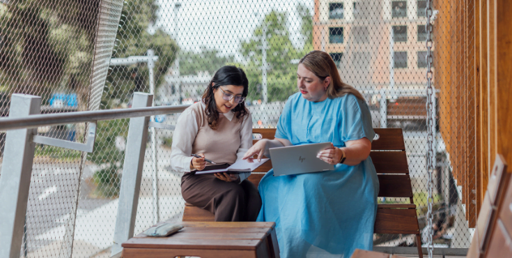 Two alumni discussing ways to advance their careers. One is holding a laptop and the other a notebook.