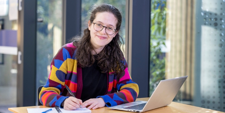 A female student working on a research project with a laptop and notebook.