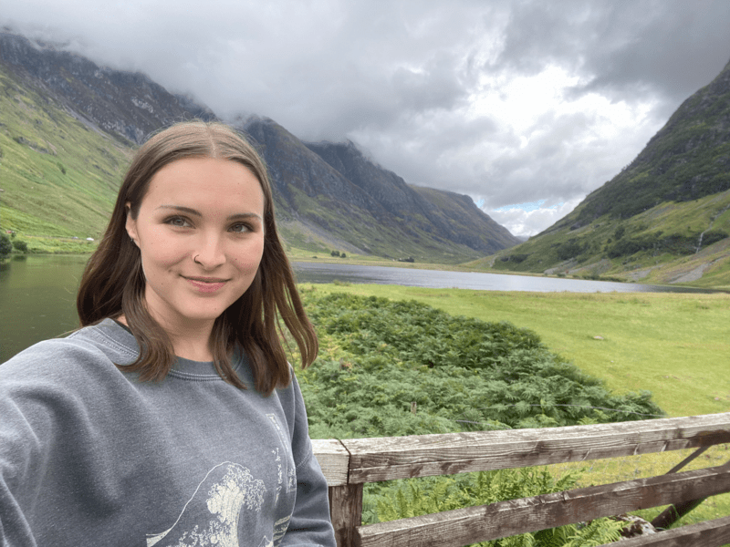 Margot smiling with a beautiful backdrop against lush greenery and foggy mountains.