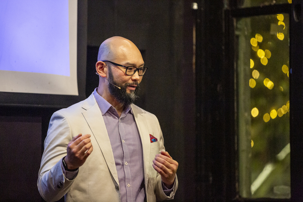 A man with a beard and glasses speaking to a group during a presentation.