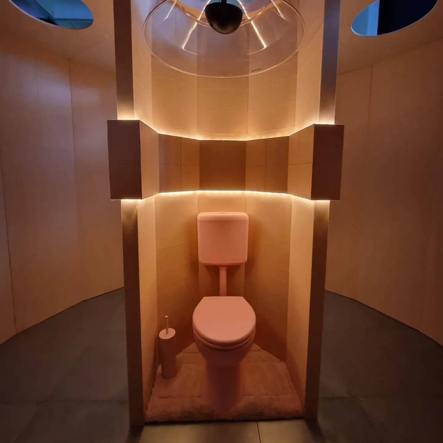 A pink toilet in a pink cubicle with soft, warm lighting