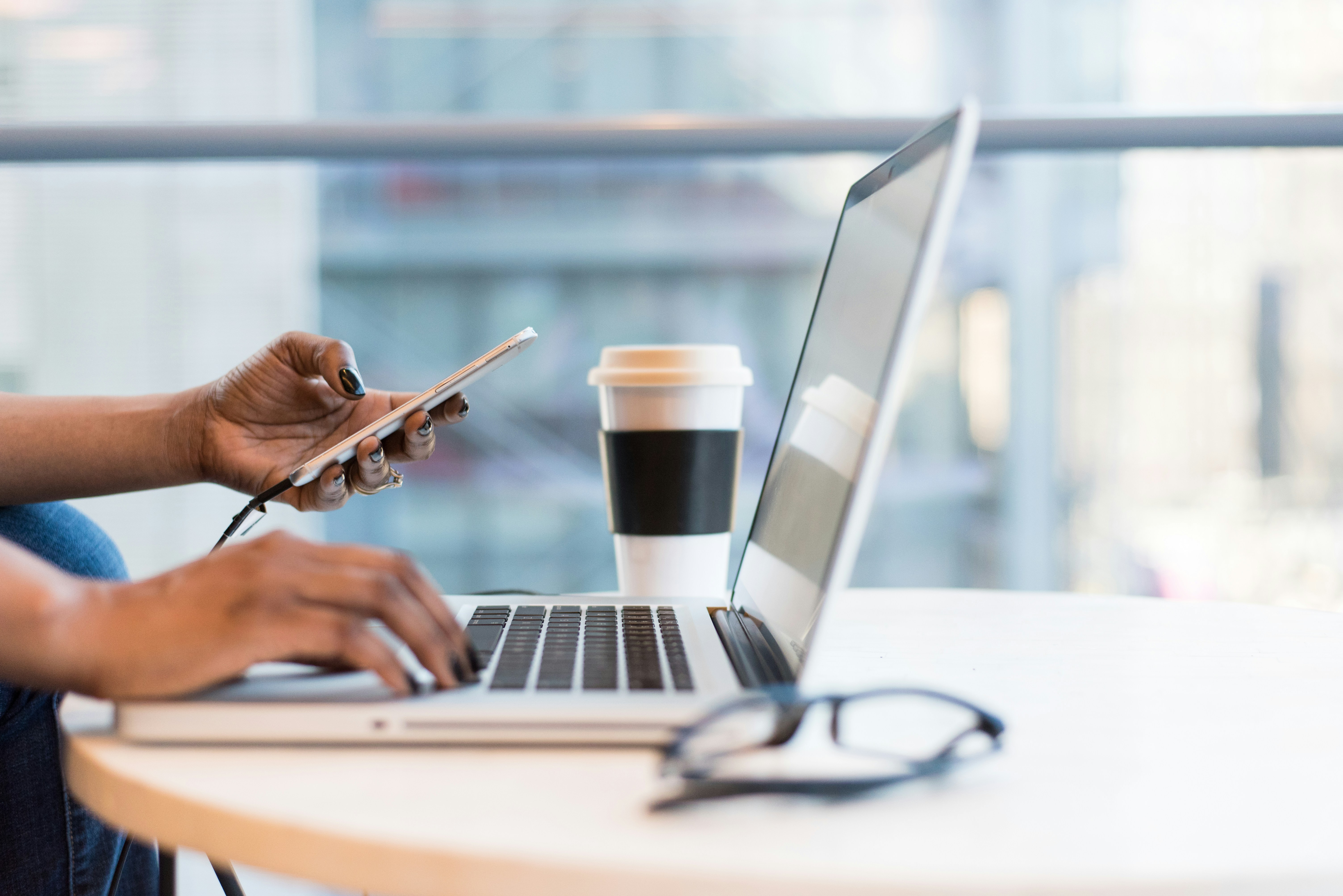 Person pictured working with laptop while holding phone. 