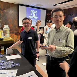 Two alumni at a Perth Alumni Network event finding their nametags at a table.
                                class=