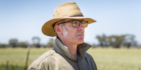 Image of a male researcher weating a hat, standing in a field.