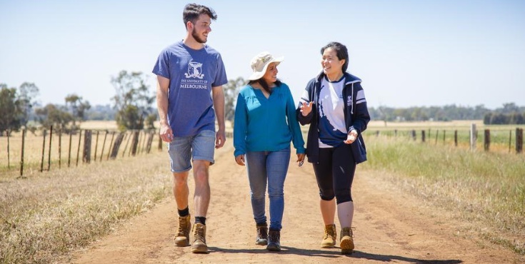 Three University community members walking down a dirt road in a rural location.