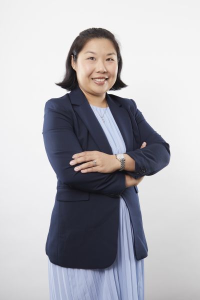 Person standing with arms crossed against a plain light background, wearing a dark blazer over a light‑coloured outfit
