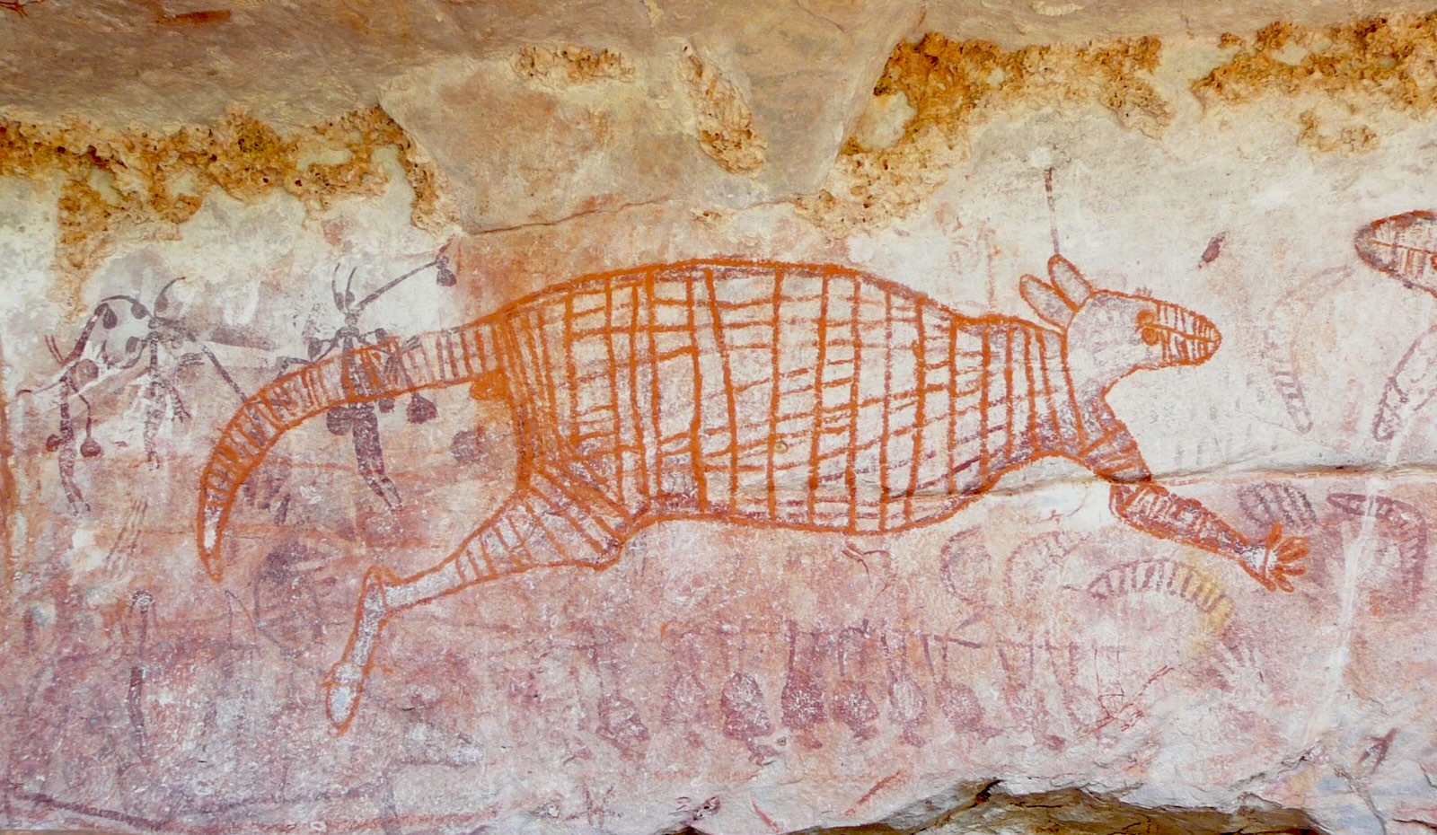 Rock art using red and other ochres on a cave siding, depicting a kangaroo, tools and other figures
