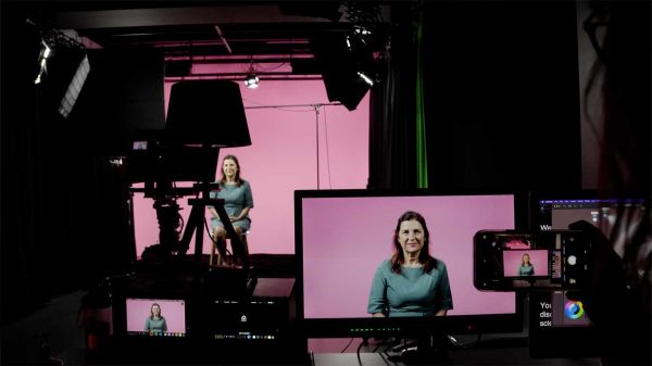 A woman presents to camera in a pink-lit film studio.