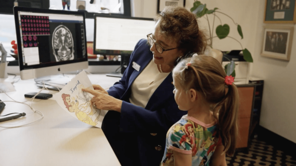 A woman and a young girl sit together at a desk, looking at a cartoon drawing.