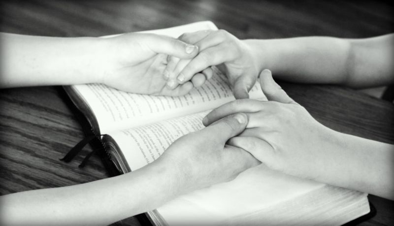 Image of two people holding hands in prayer.