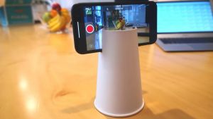 An upside down paper cup with the slot cut into the top where a phone is positioned.