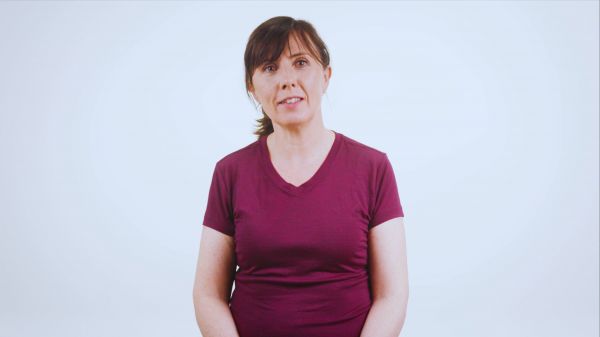 A woman with dark hair and a maroon v-neck tee-shirt stands against a plain white studio background.