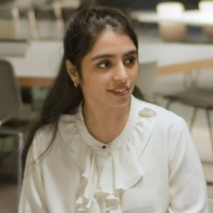 A female student wearing a white blouse smiling into the distance.
                                class=