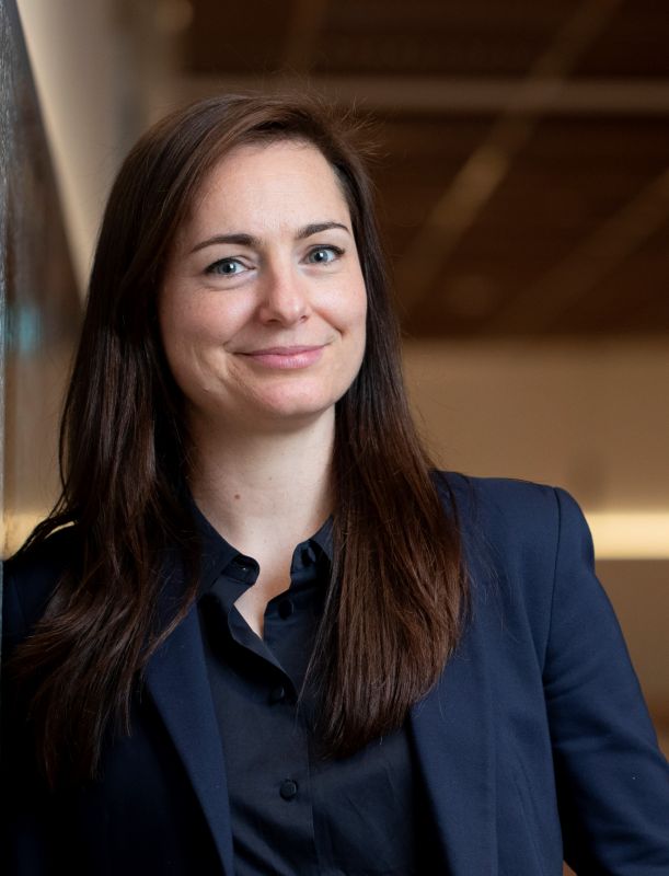 A dark haired woman wearing a blue suit with a modern office backdrop