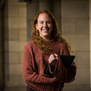 Photo of Laura in a brown sweater and clutching a laptop.
                                class=