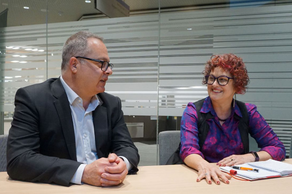 Two people sitting beside each other at a boardroom table having a conversation.