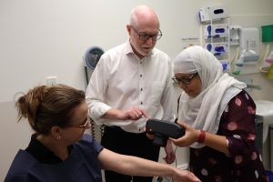 Dr Noor E Karishma Shaik demonstrating AI-powered skin cancer detection on research participant, Sarah Chivers, while Associate Professor Peter Foley observes. The team is developing a more accessible prototype through this pilot study.