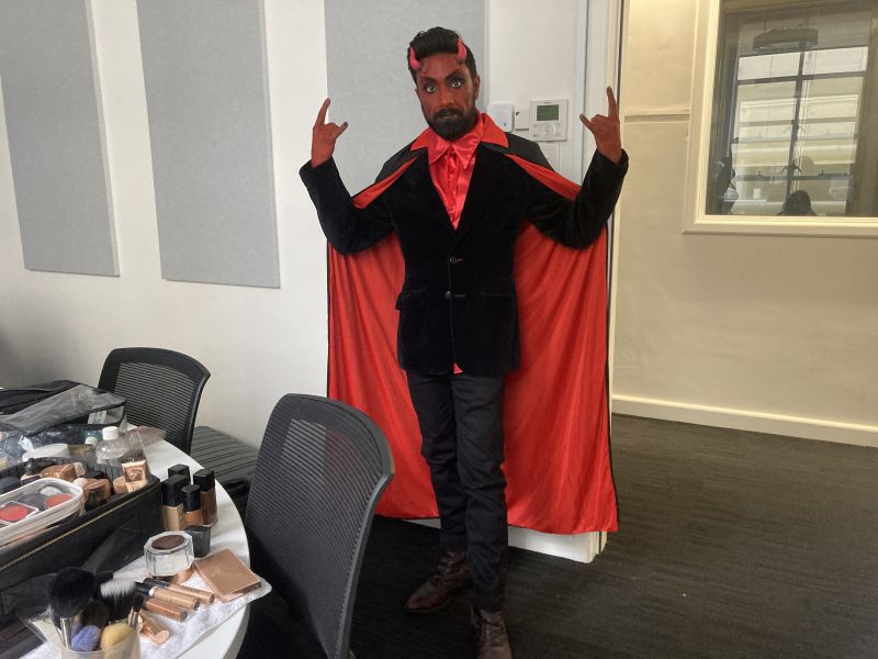 A man dressed as a devil poses in front of an office wall.