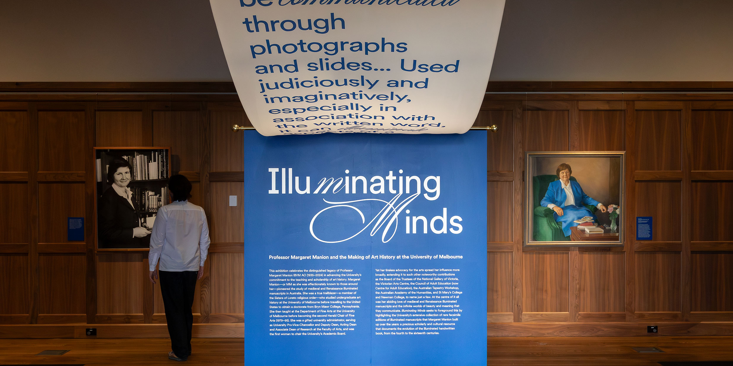 A person looks at an artwork in a gallery with a big blue banner in foreground with the text Illuminating Minds