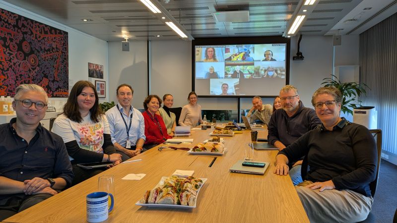 People gathered around a table in a meeting room with a video call on screen