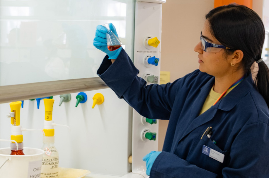 A person with a ponytail in a laboratory holding up a glass beaker