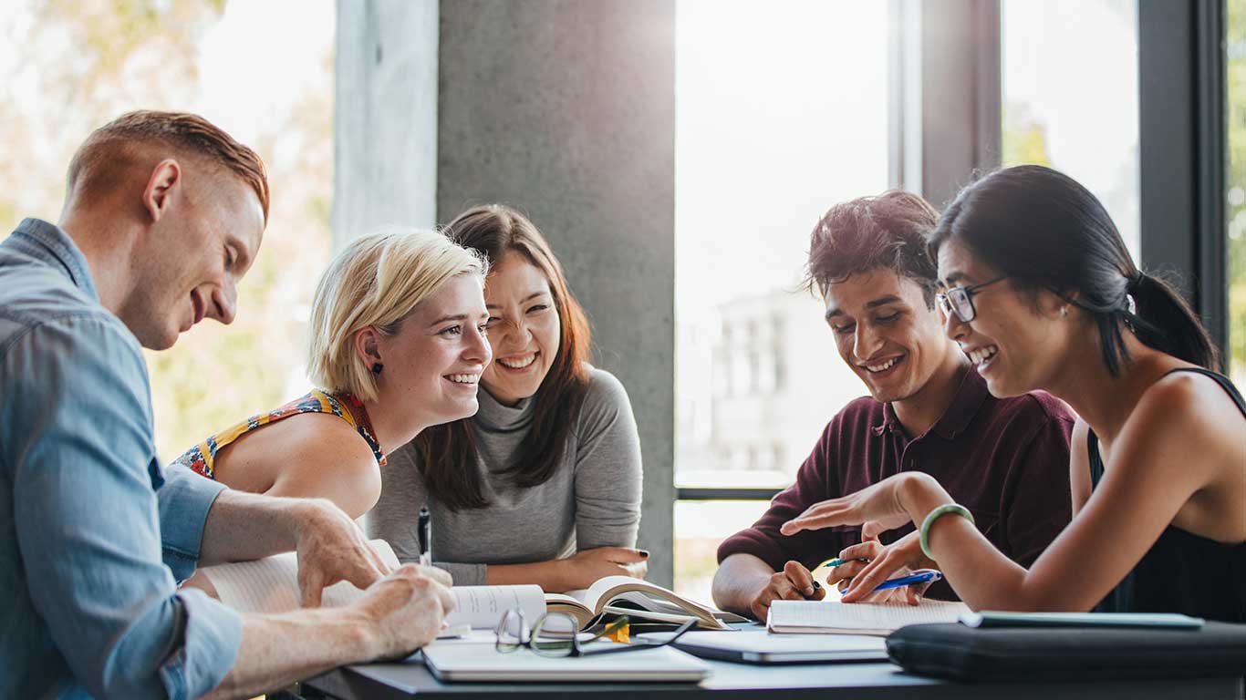 A group of students sit around a table talking and laughing as they study.