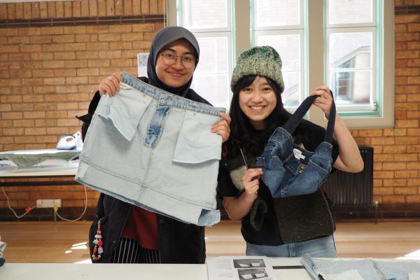 Two students hold up tote bags made from old jeans