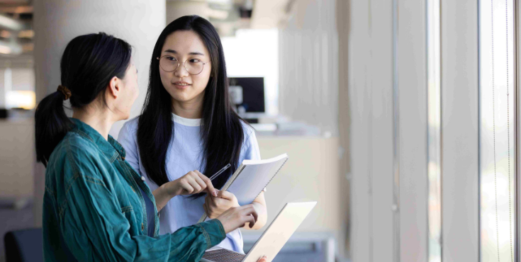 A mentor holding their laptop while speaking with their student mentee.