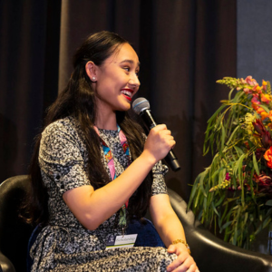 Image of Mahsa speaking through a microphone at an event.
                                class=