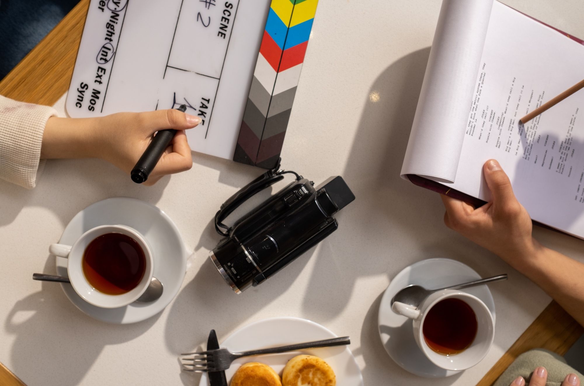 Hands on a table with coffee and snacks looking through a script for a video shoot.